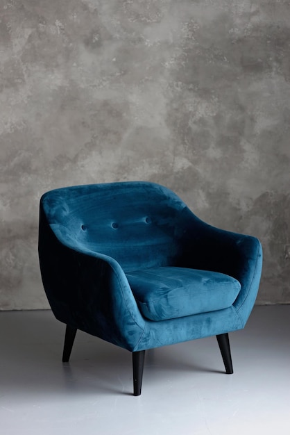 Classic blue velvet art deco armchair with wooden legs against a gray wall Front view Soft selective focus