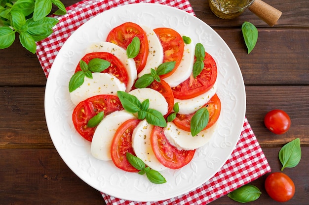 Classic caprese salad with mozzarella cheese tomatoes and basil on a white plate Top view