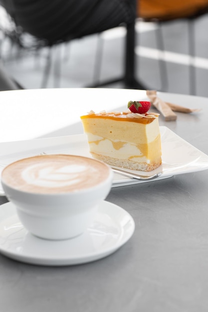 Classic cheesecake with fresh strawberry with cup of coffee on white table. Close Up view. Tasty breakfast. Piece of cake on plate, white cup on white marble background.