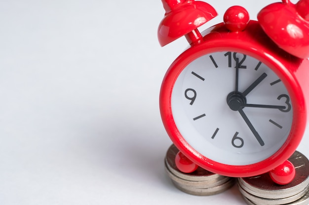 Classic clock on a stack of coins on white