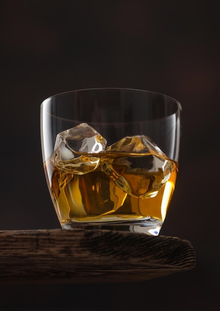 Classic glass of scotch whiskey with ice cubaes on top of wooden board and black background