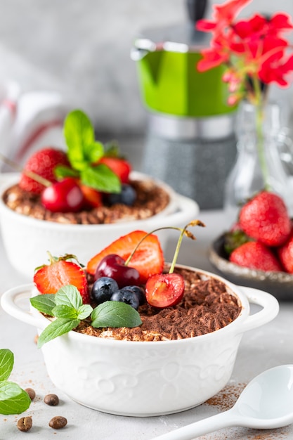 Classic Italian dessert Tiramisu decorated with strawberries, cherries and mint on a white background.