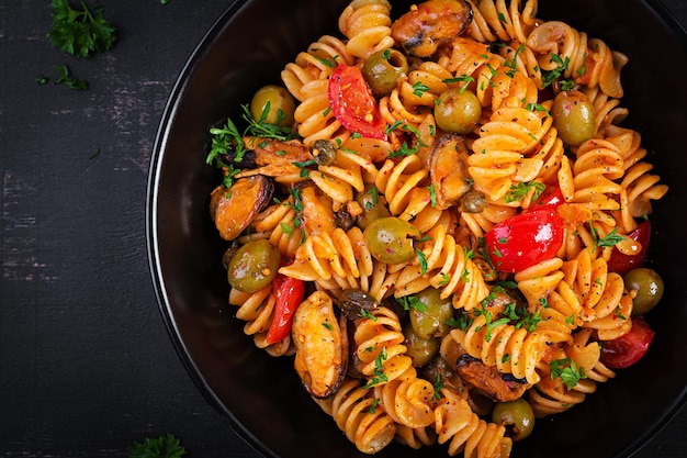 Classic italian pasta fusilli marinara with mussels green olives and capers on dark table Fusilli pasta with sauce marinara Top view overhead