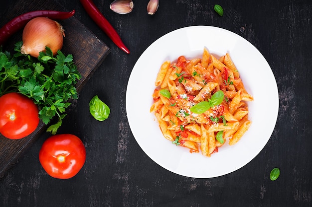 Classic italian pasta penne alla arrabiata with basil and freshly grated parmesan cheese on dark table. Penne pasta with chili sauce arrabbiata. Top view, above, copy space