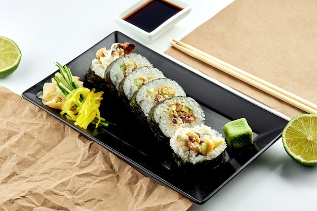 Classic Japanese sushi roll - futomaki with cucumber, cream cheese and baked salmon, served in a black plate. White surface