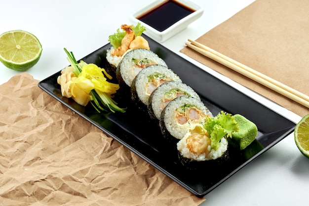 Classic Japanese sushi roll - futomaki with cucumber, cream cheese and tempura shrimp, served in a black plate. White surface