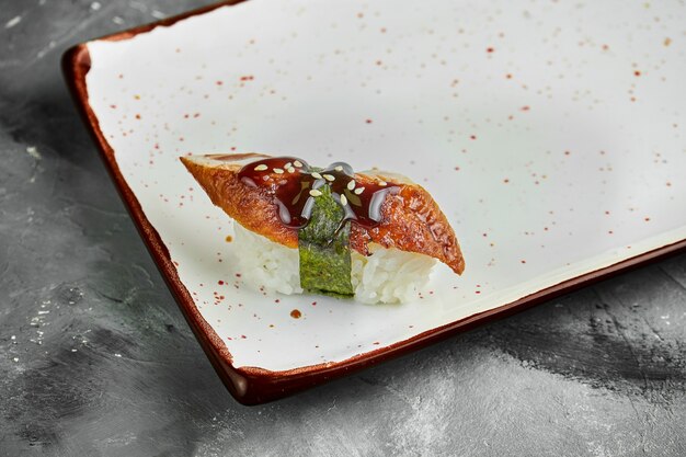 Classic Japanese sushi with eel, unagi, sesame seeds and nori on a white plate on a gray table. Japanese cuisine. Close up, selective focus