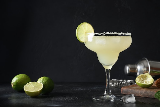 Classic margarita cocktail with lime juice and ice cube on dark black background with copy space