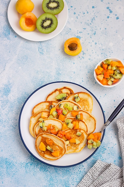 Classic pancakes garnish with apricot, kiwi and mint on ceramic plate