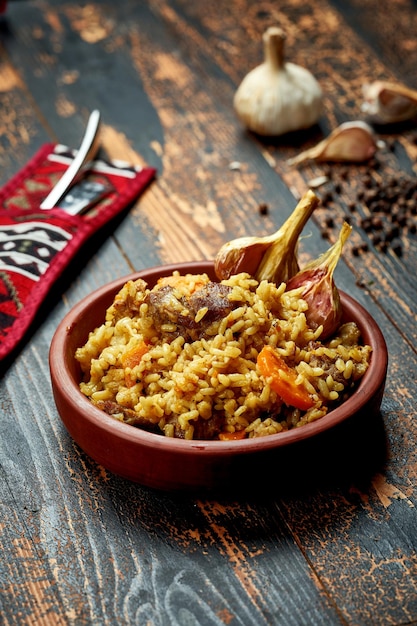 Classic pilaf with beef garlic and carrots in a clay plate on a wooden background Rustic