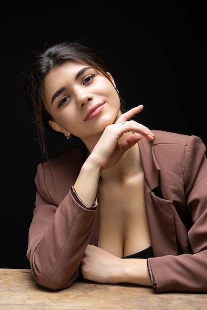 Classic studio portrait of a young brunette dressed in a black top and formal suit who is sitting on a chair against a black background