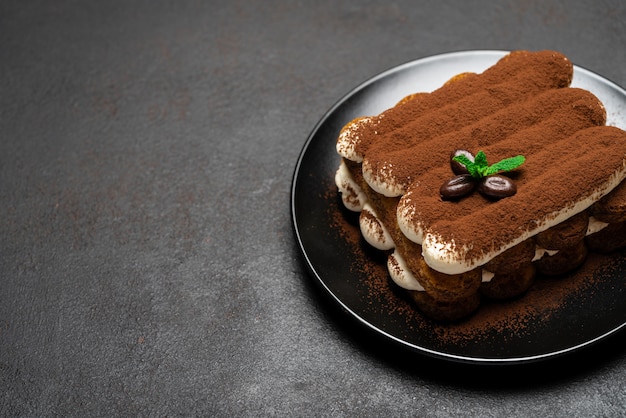 Classic tiramisu dessert on ceramic plate on dark concrete surface