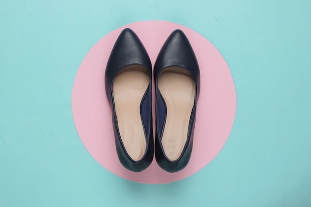 Classic womens high heel shoes on a blue paper with a pastel pink circle in the middle