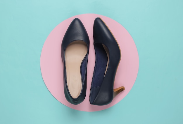 Classic womens high heel shoes on a blue paper with a pastel pink circle in the middle