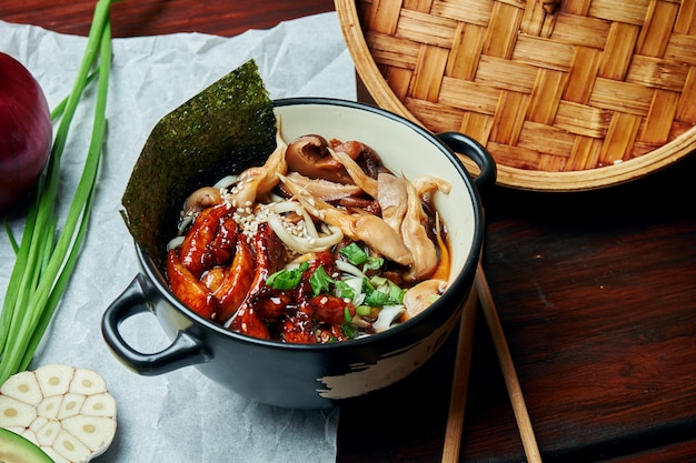 Classical Asian soup with udon noodles, nori, shiitake mushrooms, and wok-fried chicken in black bowl on wooden table with copy space. Top view, flat lay food