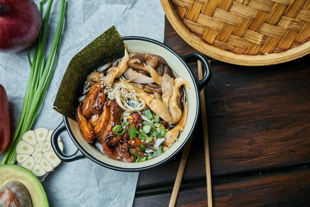 Classical Asian soup with udon noodles, nori, shiitake mushrooms, and wok-fried chicken in black bowl on wooden table with copy space. Top view, flat lay food