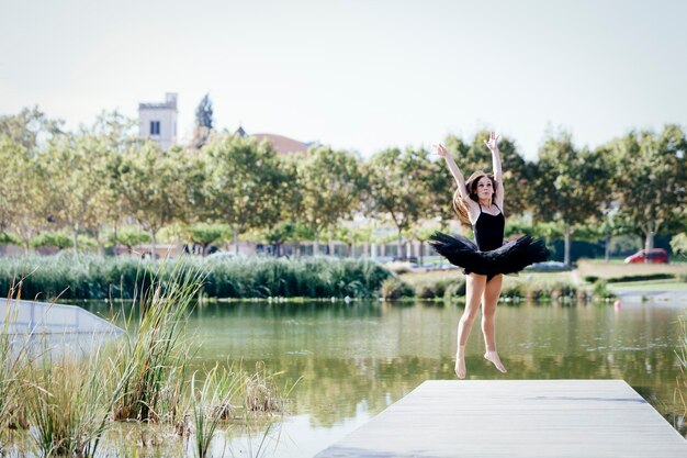 Classical ballerina jumping on a footbridge of an urban lake on a sunny day