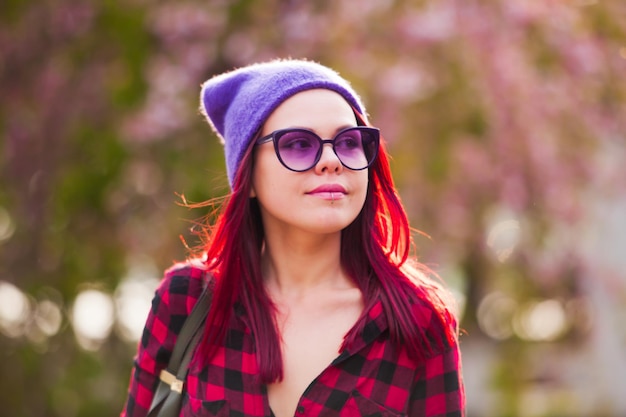 Classy young woman with bright fuchsia colored hair looking away through purple glasses. Colorful life concept. Blured city on a background