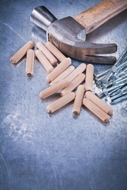 Claw hammer heap of construction nails and wooden dowels on scratched metallic background maintenance concept