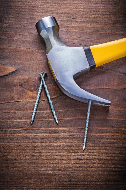 Claw hammer with yellow handle and nails on vintage wooden board