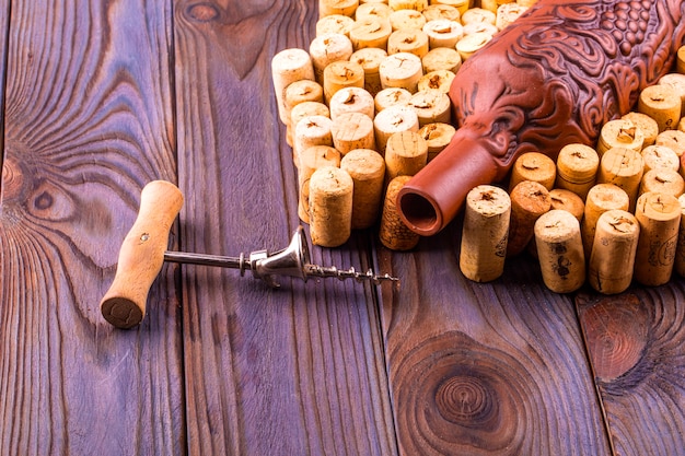 Clay bottle, metal corkscrew and cork on a wooden table.