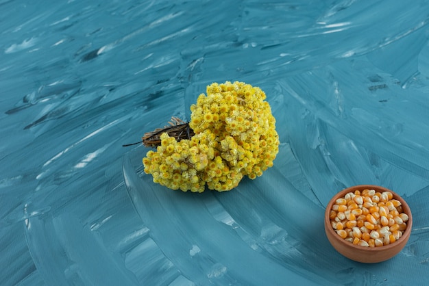 A clay bowl full of uncooked corn seeds with bouquet of flower .