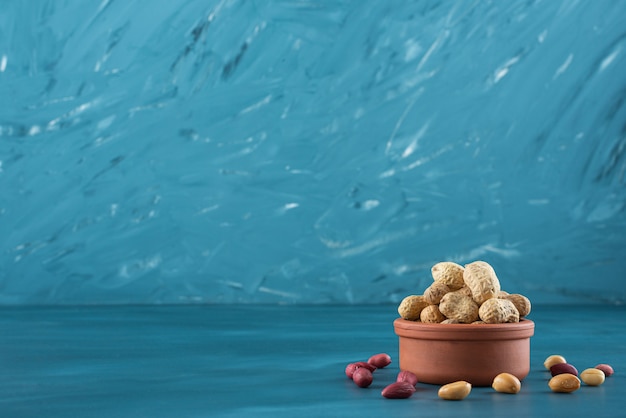 Clay bowl of shelled raw peanuts on blue table.