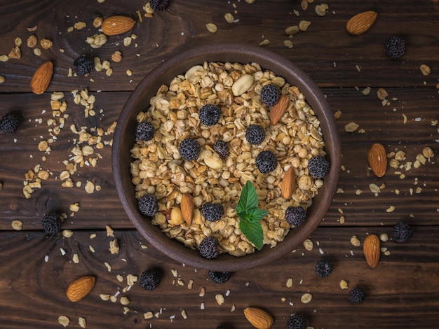 A clay bowl with granola berries and nuts on a wooden table