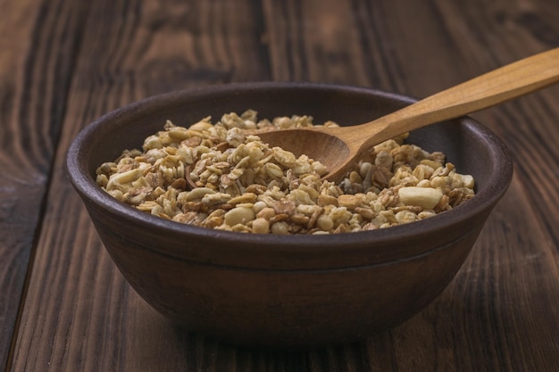 A clay bowl with granola and a wooden spoon on a wooden table