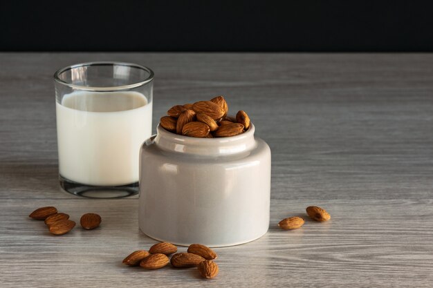 Clay jar with almonds and vegan milk on wooden table