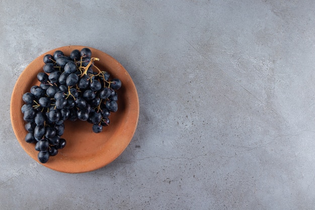 Clay plate of fresh black grapes on stone background. 