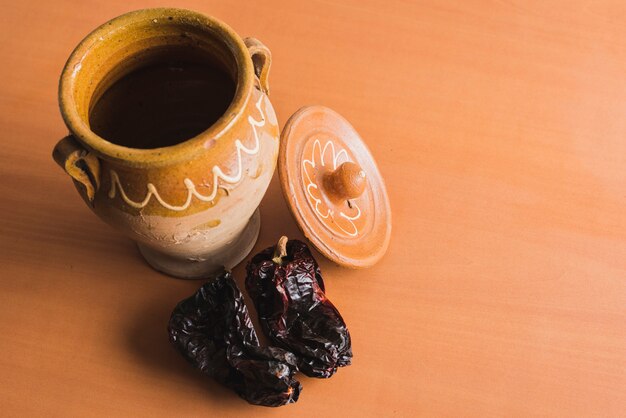 Clay pot with two dried peppers on brown wood