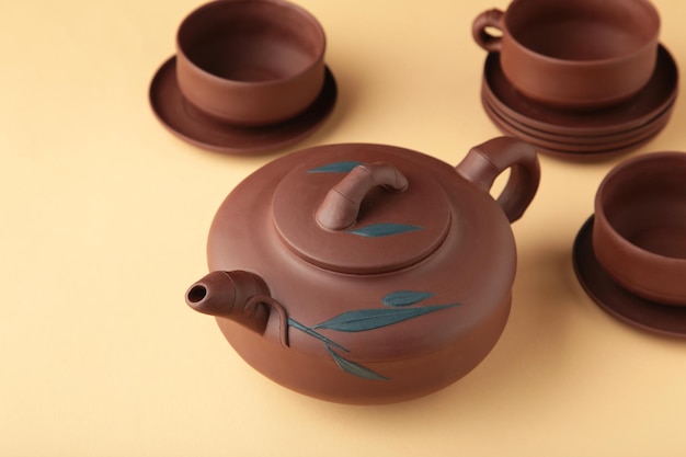 Clay teapot with cups on beige background