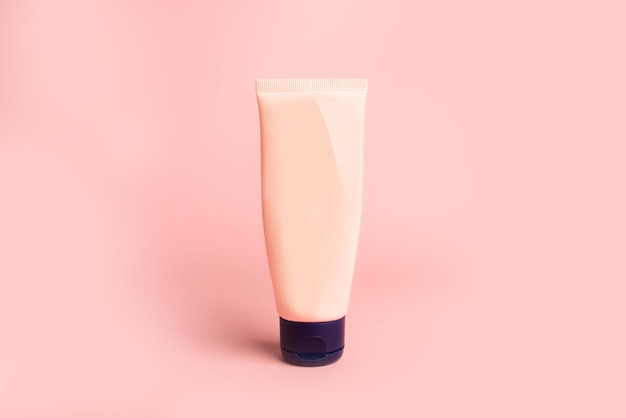 Clean beige plastic tube with face cream on pink background