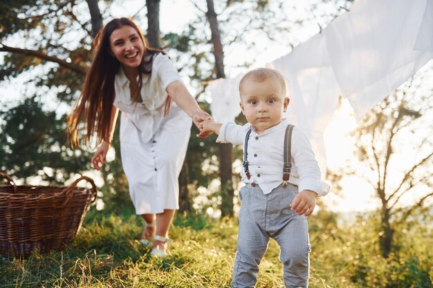 Clean clothes hanging on the rope to dry Young mother with her little son is outdoors in the forest Beautiful sunshine