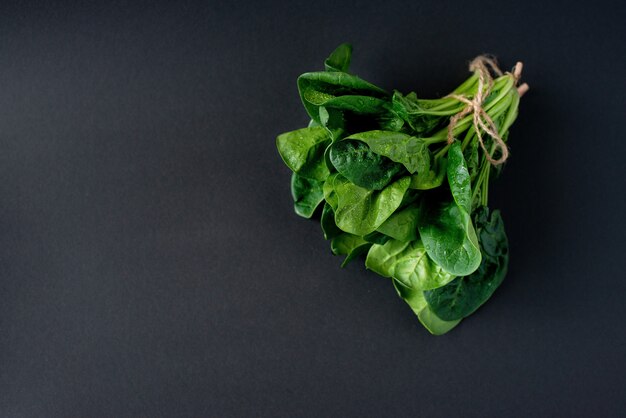 Clean food concept. Bunch of leaves of fresh organic spinach greens on a black background. Healthy detox spring-summer diet. Vegan Raw Food. Copy space.