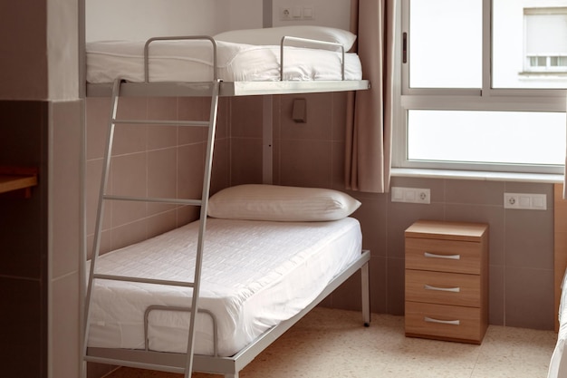 A clean and minimalistic hostel room with a bunk bed white bedding and a small wooden bedside table ideal for budget travelers seeking affordable accommodation Cheap hostels save money