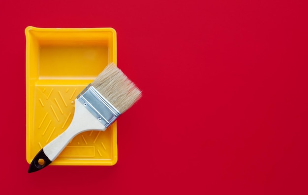 Clean paint brush and yellow plastic paint tray on a red background Copy space