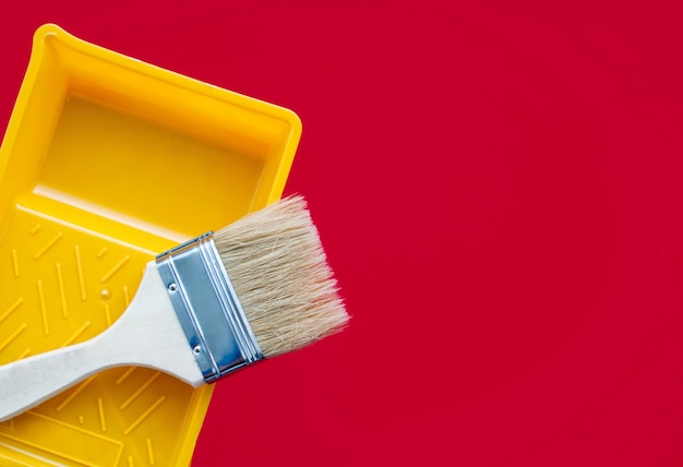 Clean paint brush and yellow plastic paint tray on a red background Copy space