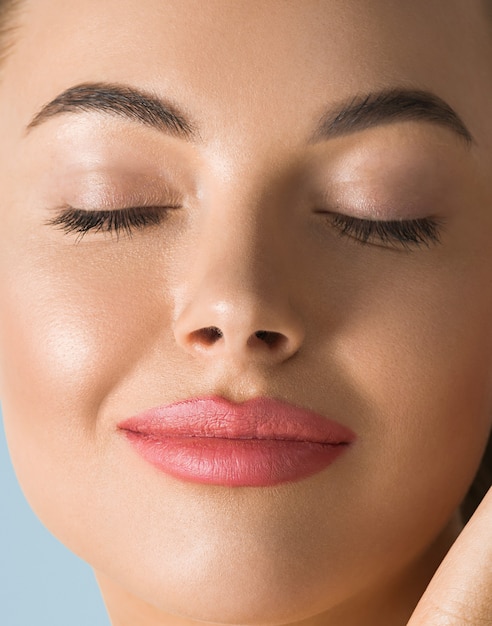 Clean skin woman face close up beauty tanned face beautiful smile. Blue background. Touching face.