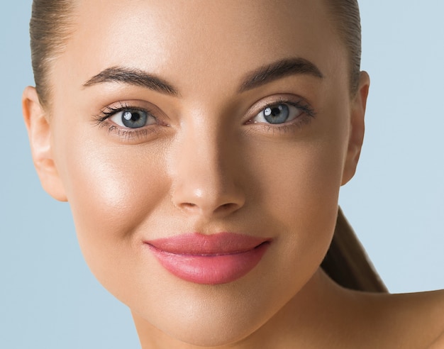 Clean skin woman face close up beauty tanned face beautiful smile. Blue background.