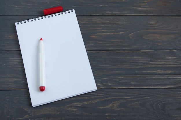 A clean white notebook page with a marker on a wooden background Space for text