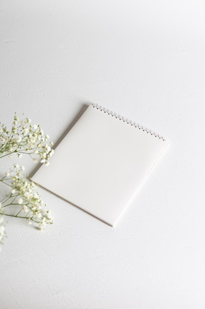 A clean white spiral notebook lies on a white structural background Side view