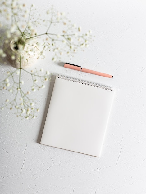 A clean white spiral notebook lies on a white structural background There is a pink pen next to it