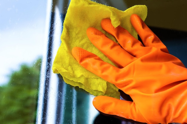 Cleaner in a glove washes a window orange yellow cloth closeup