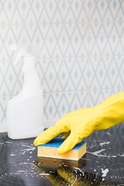 A cleaner in a yellow glove washes a kitchen stove with a sponge and foam White kitchen cleaner mockup