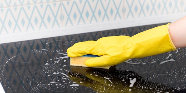 A cleaner in a yellow glove washes a kitchen utensil with detergent foam and a sponge