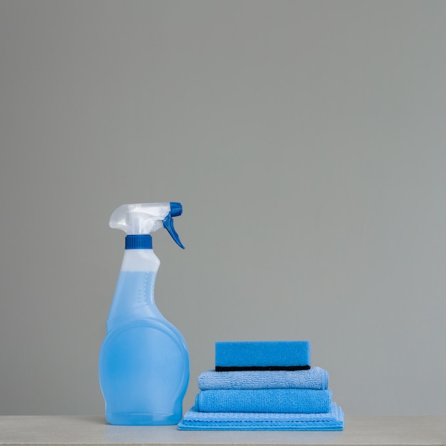 Cleaning blue spray bottle with plastic dispenser, sponge and cloth for dust  on grey background.