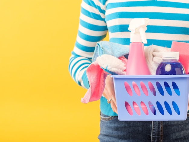 Cleaning concept. DIY home cleanup. Woman with basket of supplies. Copy space on yellow wall.