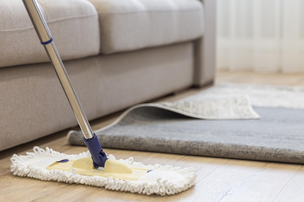 Cleaning floor with mop under carpet in living room